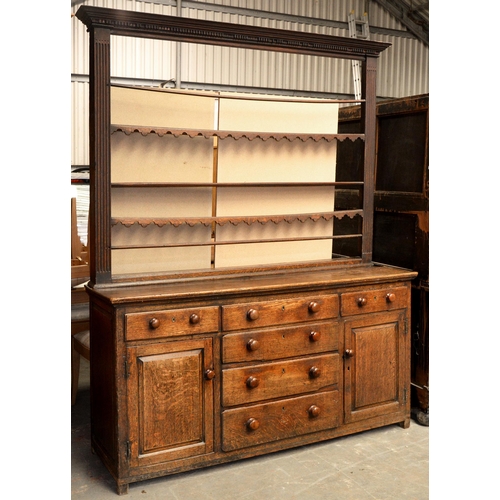 950 - A George III oak dresser, the lower part with panelled doors and boarded top, the rack with dentil c... 