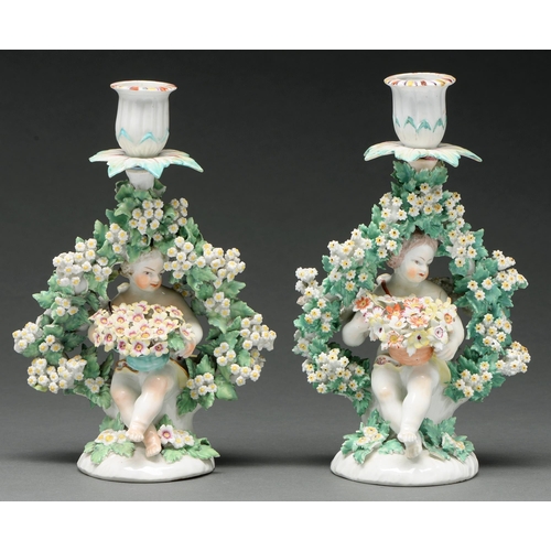 664 - A pair of Derby figural candlesticks modelled as putti, c 1770, each seated holding flowers, wi... 