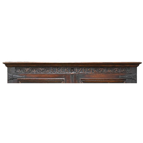 1035 - A Queen Anne oak joined clothes press, dated 1704, with moulded cavetto cornice, the frieze carved w... 