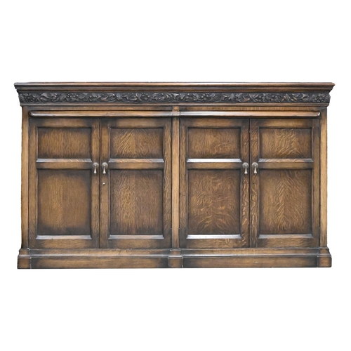 1035 - An antique style oak cupboard, the lower part enclosed by two pairs of panelled doors below a carved... 