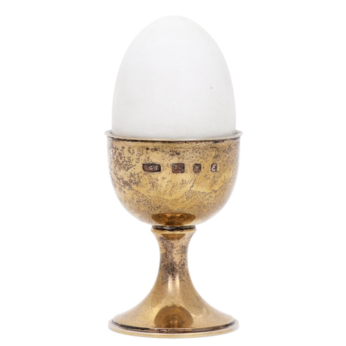 471 - Anthony Elson. An Elizabeth II silver gilt and white enamel 'surprise' egg cup and egg, containing a... 