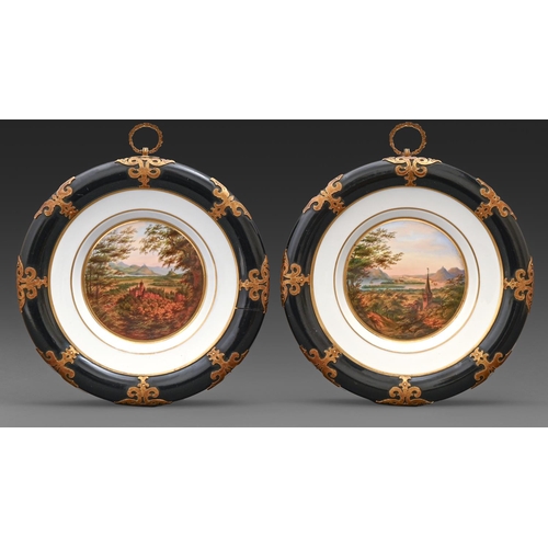 553 - A pair of German porcelain plates, c1870, painted with rural and castle views in ebonised gothic fra... 