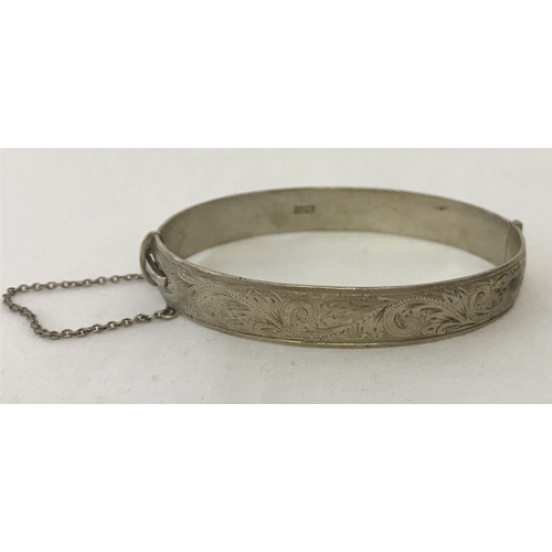 1158 - A vintage oval shaped half engraved silver bangle complete with safety chain. Hallmarked Birmingham ... 