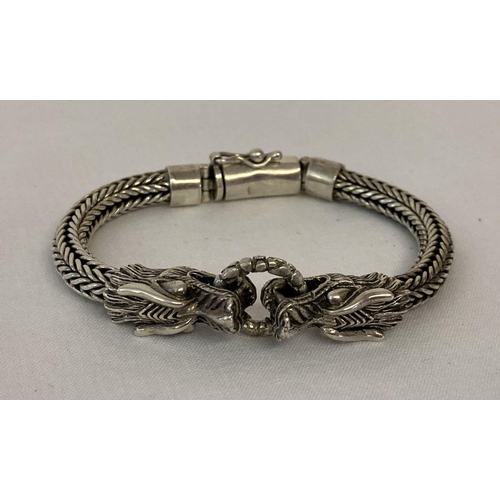 1082 - A silver double dragon head bracelet. Two dragon heads holding a silver ring. Braided wheat style ch... 