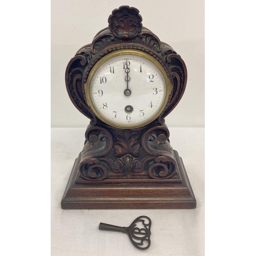 1162 - A decoratively carved wooden wind up mantel clock with enamelled face and French movement.  Complete... 