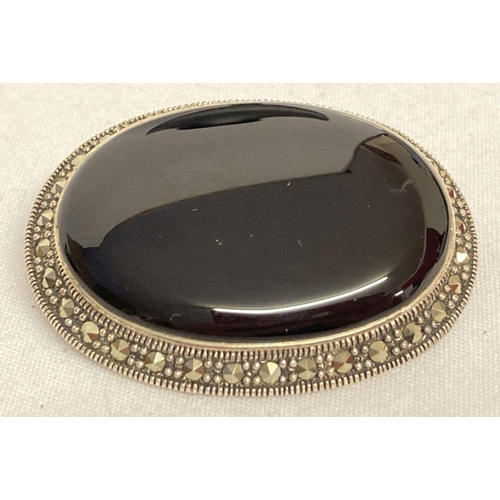 1034 - A silver pendant/brooch set with onyx and marcasite stones. Large central oval cut onyx surrounded b... 