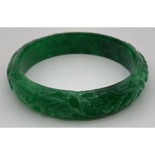 224 - A green jade bangle with carved detail to outer surface. Approx. 7.5cm diameter.