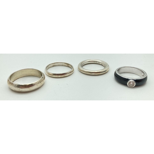 96 - 4 silver band rings. 3 plain bands together with a black enamel band ring set with a single clear st... 