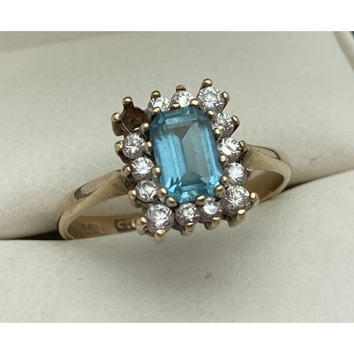 129 - A 9ct gold blue topaz and clear stone dress ring. A square cut central blue topaz surrounded by smal... 