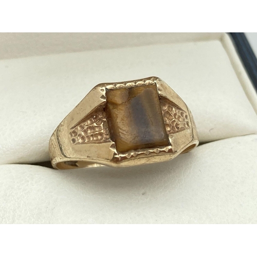 147 - A 9ct gold signet ring set with a square cut tigers eye stone. Hammered gold detail to shoulders. Ri... 