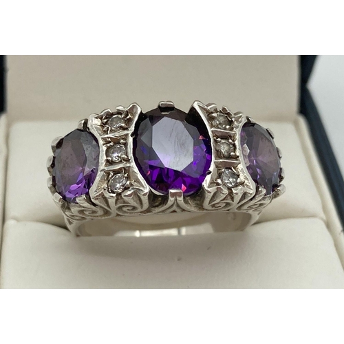 193 - A silver cocktail ring set with 3 oval cut purple stones and 6 small round cut clear stones. Scroll ... 