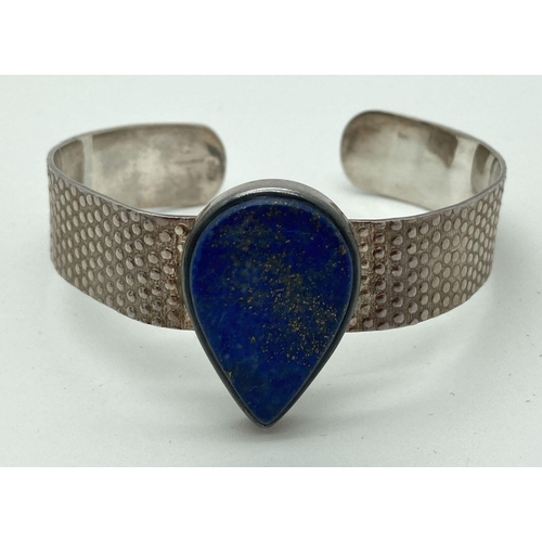 194 - A modern design silver cuff bangle with embossed design and central teardrop lapis lazuli stone. Ins... 