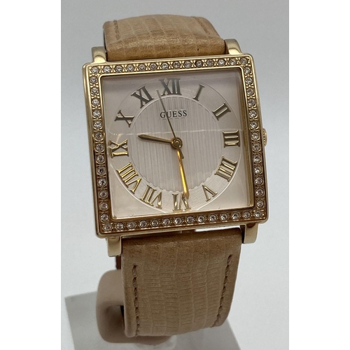 311 - A ladies Guess wristwatch with nude leather strap. Square gold tone case set with clear crystal ston... 