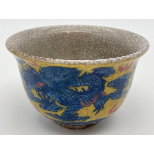 1204 - A Chinese crackle glaze ceramic tea bowl. Yellow ground with blue dragon & phoenix design to outer b... 