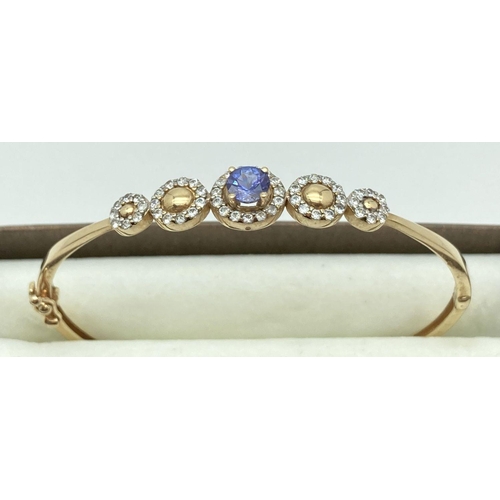 3 - A 14ct gold hinged bangle with stone set flower design to top. Central oval iolite stone surrounded ... 