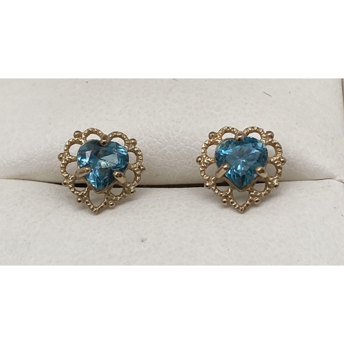 141 - A pair of pierced work heart shaped gold earrings each set with a round cut blue topaz stone.  Total... 