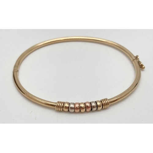 13 - A 9ct yellow gold hinged bangle with tri-coloured gold beaded detail. With fold over clasp, marked 3... 