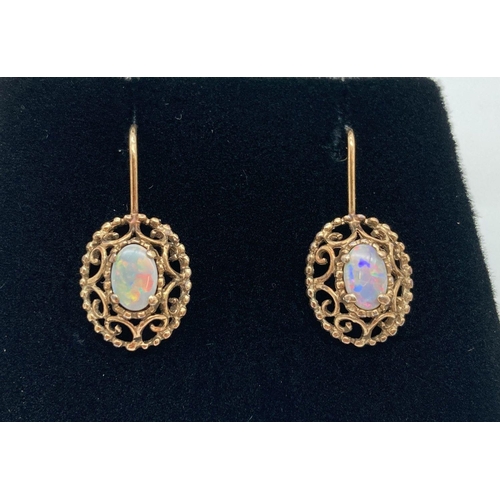 22 - A pair of 9ct gold and opal drop earrings with hook wires. Central oval opal (approx. 6mm x 4mm) in ... 