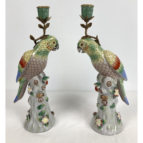 1159 - A pair of ceramic candlesticks modelled as parrots sitting atop a stump. With flower and insect appl... 