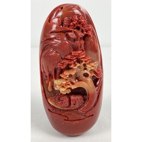 1202 - An oriental red coloured stone with carved scenic detail to one side. Depicting a boat on a river wi... 