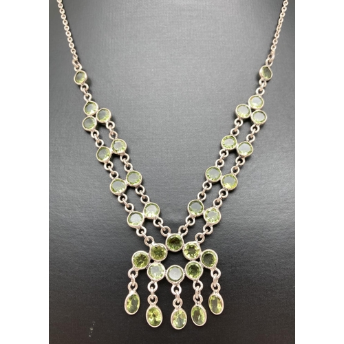 1102 - A fixed drop pendant style decorative silver necklace with 33 round and oval cut peridot stones. Lob... 