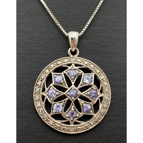 1023 - A modern design pierced work circular shaped pendant set with tanzanite's & diamonds. On an 18