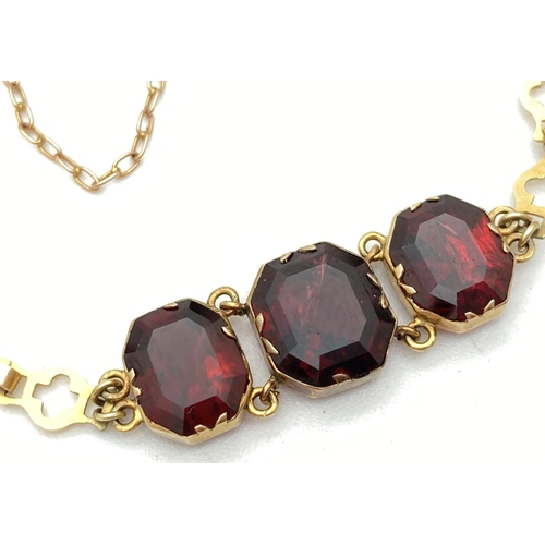 1123 - A 9ct gold linked 3 stone bracelet set with garnets. With push box clasp and safety chain. Tests as ... 