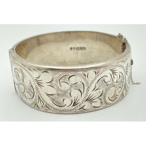 1149 - A vintage silver wide, half engraved, hinged bangle with push fastening & safety chain (broken). Eng... 