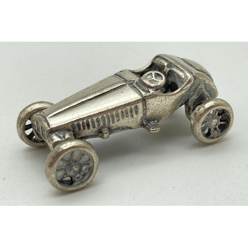 1215 - A miniature silver model of veteran racing car, with moving wheels. Stamped to underside '975 AR'. A... 