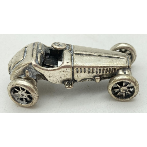 1215 - A miniature silver model of veteran racing car, with moving wheels. Stamped to underside '975 AR'. A... 