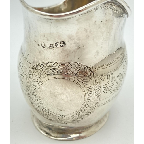 1219 - A Georgian silver cream jug with engraved floral banded design. Featuring a wreathed circular shaped... 