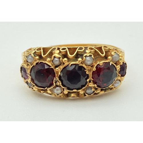 1027 - A Victorian 15ct gold ring with decorative mount set with garnets and seed pearls. Engraved detail t...