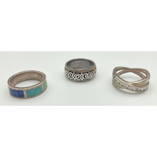 1069 - 3 silver band style rings. A crossover style set with clear stones, a decorative band with scroll de... 