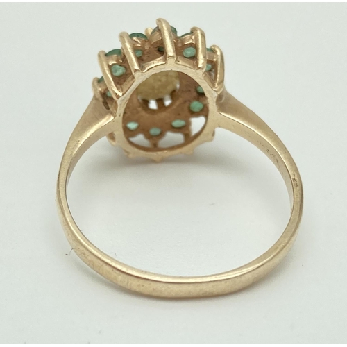 1009 - A 9ct gold ring set with central oval opal surrounded by a row of 12 emeralds. Fully hallmarked insi... 