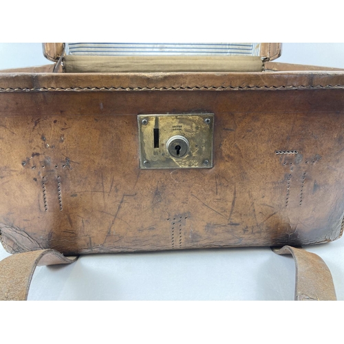 1383 - An antique leather travelling trunk with brass fixings, leather fastening straps and carry handle. B... 