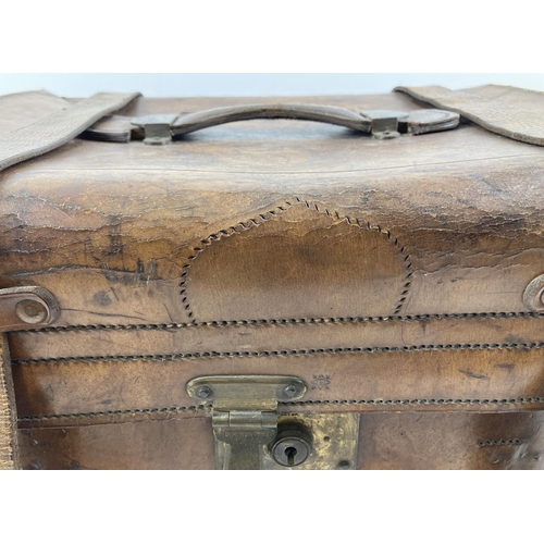 1383 - An antique leather travelling trunk with brass fixings, leather fastening straps and carry handle. B... 