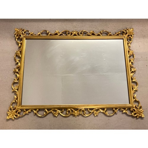 1434 - A large modern decorative gilt framed wall mirror of scroll & foliate design. Approx. 79cm x 109cm