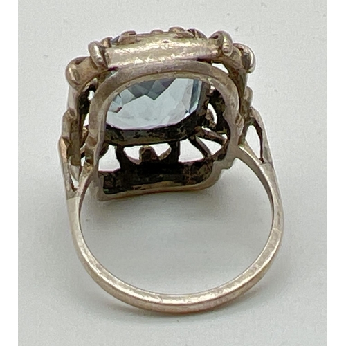 1071 - A continental silver cocktail ring set with an emerald cut pale blue spinel stone. Pierced work moun... 