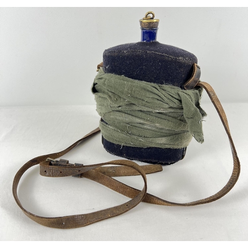 184 - A vintage blue enamelled water bottle with Navy blue felt cover, brown leather strap and brass fixin... 