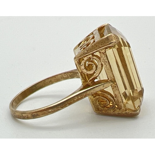 1061 - A 9ct gold cocktail ring set with a large emerald cut citrine stone. Pierced work scroll detail to m... 