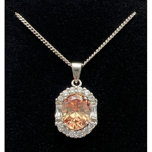 1047 - A 925 silver oval shaped pendant set with a central pale orange cubic zirconia surrounded by 12 roun... 