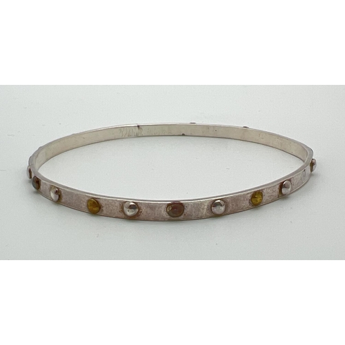 1075 - A silver modern design slim bangle with multi coloured metal studded detail. Full hallmarks to insid... 