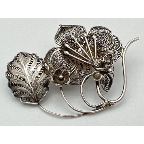 1092 - A vintage 800 silver filigree brooch in a flower spray design with butterfly detail. Pull clip faste... 