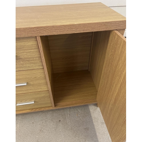 1296 - A modern light wood effect, sideboard with 2 cupboards and 3 central drawers. Long silver coloured h... 