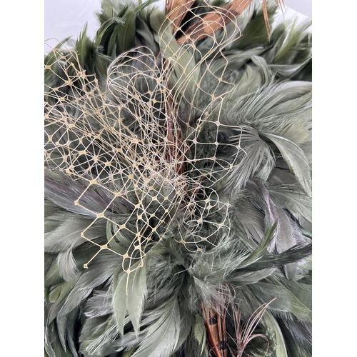 1323 - A green feather fascinator style hat with pheasant feather and net detail. Together with a Harvey Ni... 