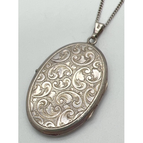 1055 - A vintage silver oval shaped locket with floral decoration to front and back. On a 24 inch fine curb... 