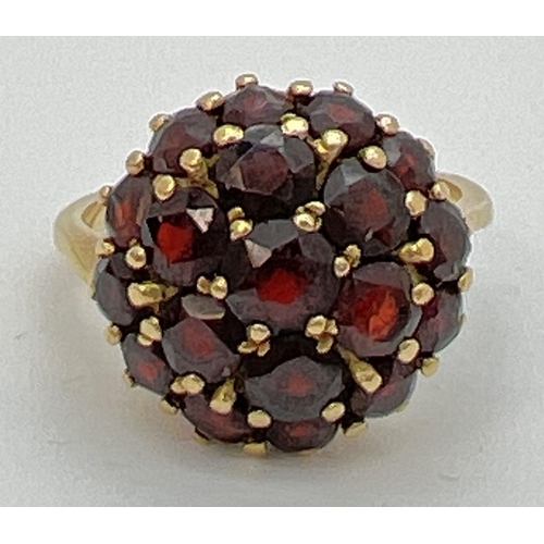 74 - A vintage 18k gold garnet set cluster style ring. Central garnet surrounded by 6 round cut garnets a... 