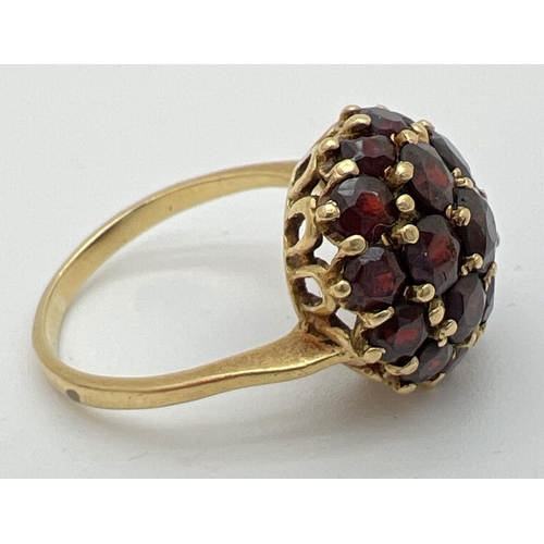 74 - A vintage 18k gold garnet set cluster style ring. Central garnet surrounded by 6 round cut garnets a... 