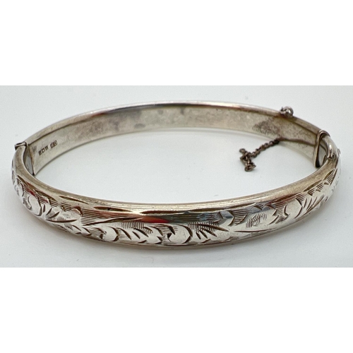 81 - A vintage silver hinged bangle with half floral engraved decoration. Safety chain needs attention. H... 