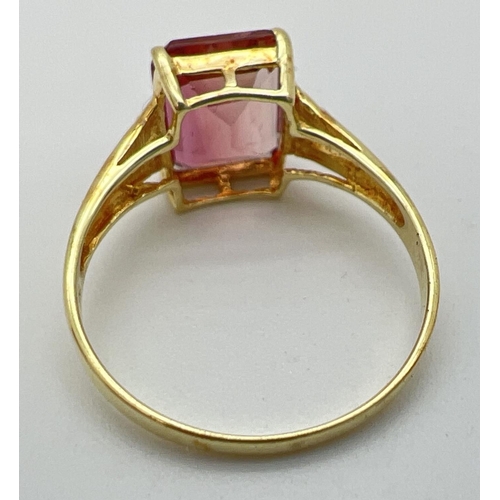 39 - A 14K gold ring set with an emerald cut blush tourmaline and two small round cut diamonds to each sh... 